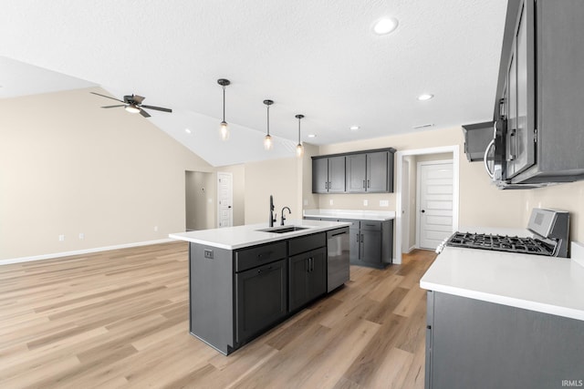 kitchen featuring appliances with stainless steel finishes, decorative light fixtures, sink, light hardwood / wood-style floors, and a center island with sink