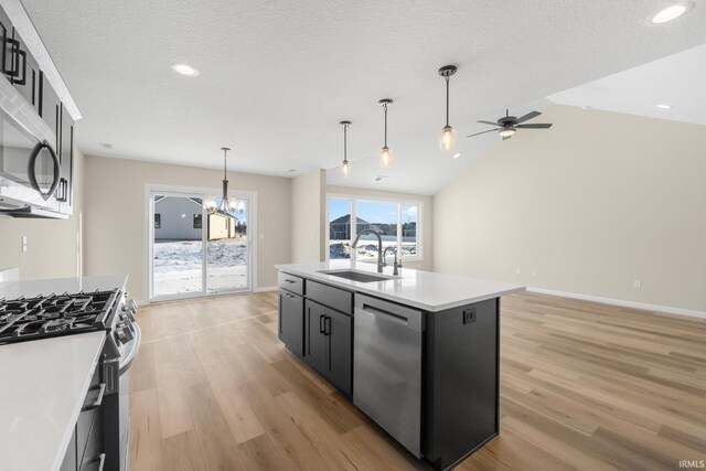 kitchen with an island with sink, sink, hanging light fixtures, stainless steel appliances, and a textured ceiling