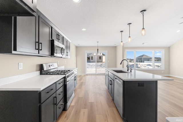 kitchen with appliances with stainless steel finishes, decorative light fixtures, sink, light hardwood / wood-style floors, and a center island with sink