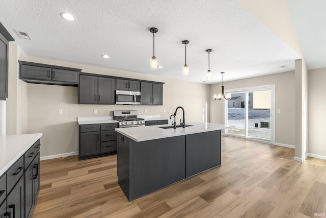 kitchen featuring pendant lighting, sink, light hardwood / wood-style flooring, appliances with stainless steel finishes, and an island with sink