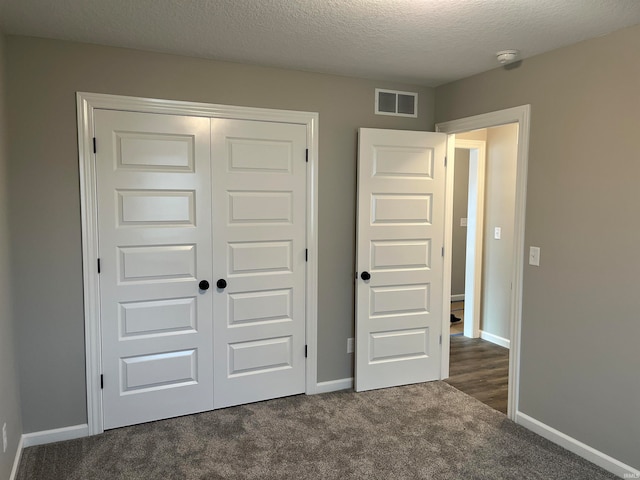 unfurnished bedroom featuring a textured ceiling, a closet, and dark carpet