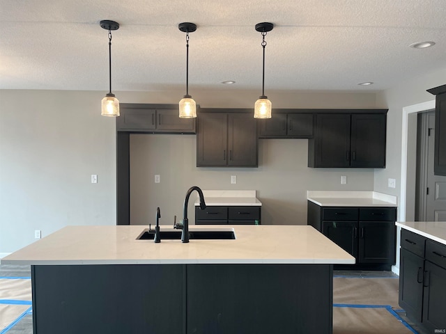 kitchen with sink, an island with sink, hanging light fixtures, and a textured ceiling