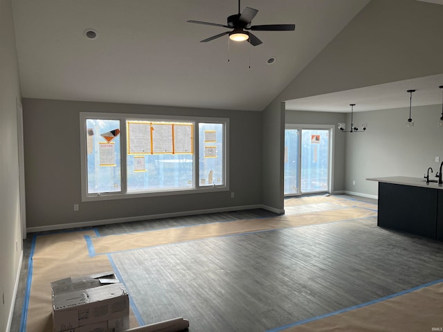 unfurnished living room with ceiling fan with notable chandelier and high vaulted ceiling