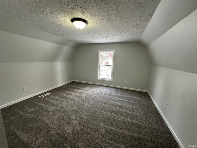 additional living space with dark colored carpet, a textured ceiling, and lofted ceiling