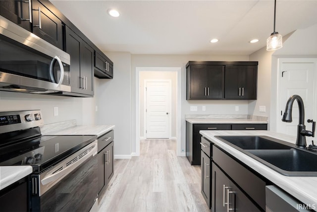 kitchen featuring light wood-type flooring, appliances with stainless steel finishes, decorative light fixtures, and sink