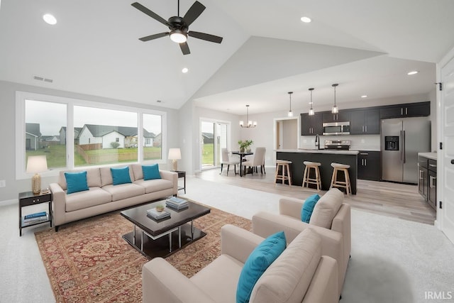 living room featuring ceiling fan with notable chandelier, light hardwood / wood-style floors, high vaulted ceiling, and sink