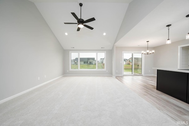 unfurnished living room with ceiling fan with notable chandelier, light wood-type flooring, high vaulted ceiling, and plenty of natural light