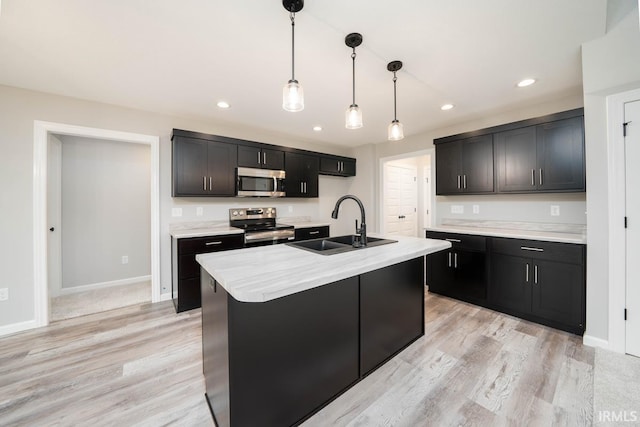 kitchen with pendant lighting, sink, a kitchen island with sink, appliances with stainless steel finishes, and light hardwood / wood-style floors