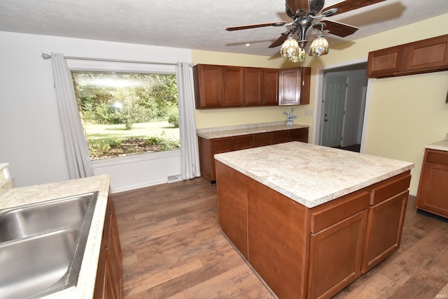 kitchen with ceiling fan, sink, a kitchen island, a textured ceiling, and dark hardwood / wood-style flooring