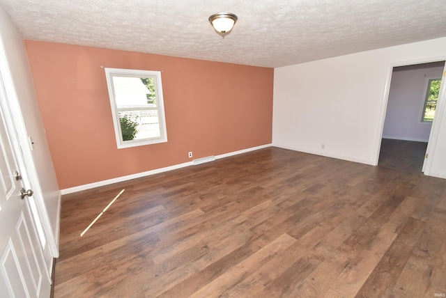 empty room with a textured ceiling, plenty of natural light, and dark wood-type flooring