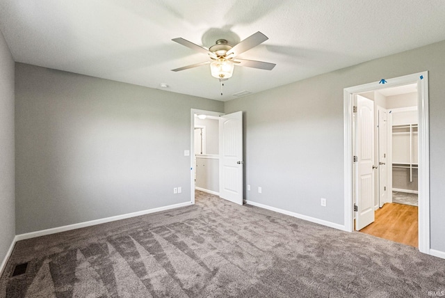 unfurnished bedroom with a spacious closet, a closet, ceiling fan, and light colored carpet