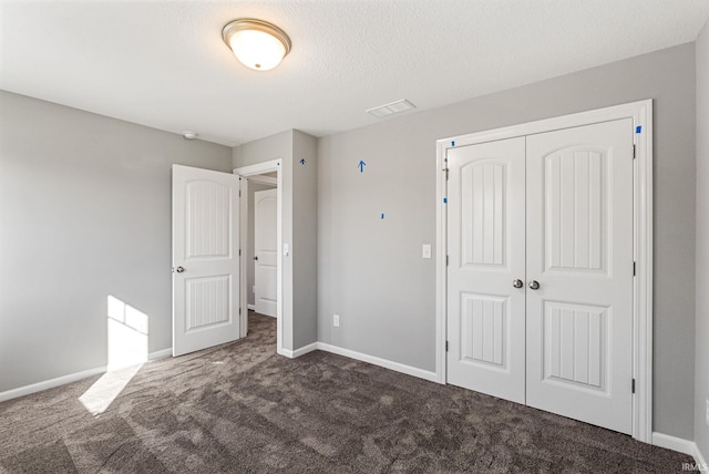 unfurnished bedroom featuring dark carpet, a textured ceiling, and a closet