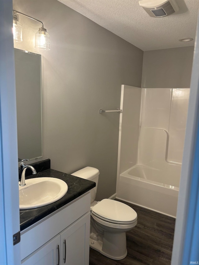 full bathroom with vanity, a textured ceiling, wood-type flooring, toilet, and  shower combination