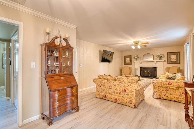 living room with light wood-type flooring, crown molding, a fireplace, and ceiling fan