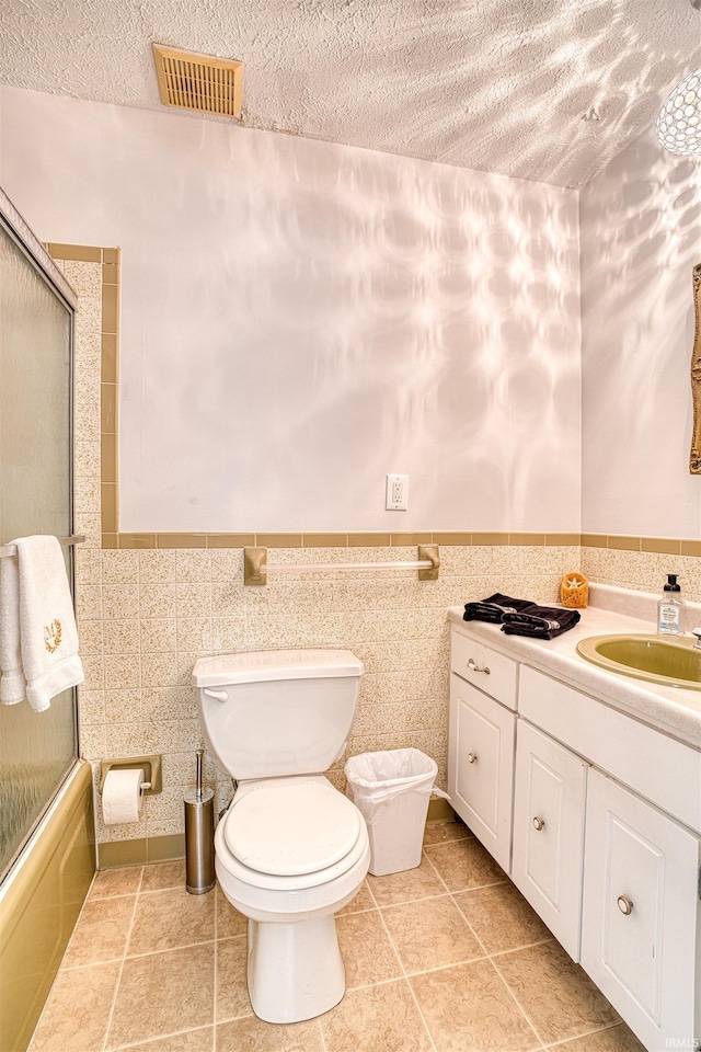 full bathroom featuring vanity, tile walls, toilet, and combined bath / shower with glass door