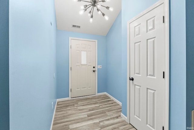 doorway to outside with light wood-type flooring and a notable chandelier