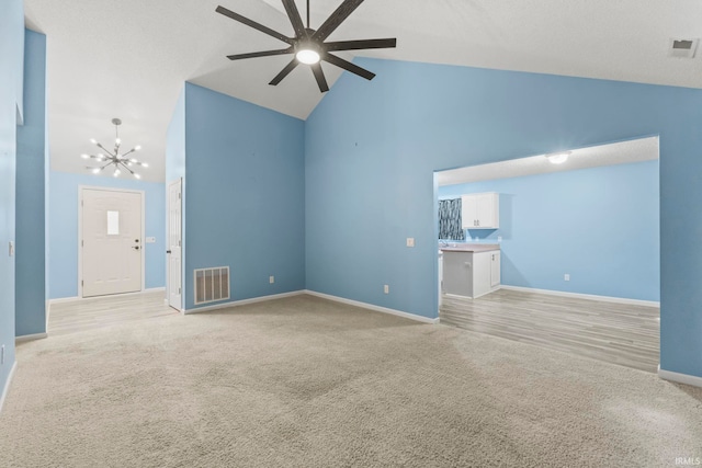 unfurnished living room with ceiling fan with notable chandelier, high vaulted ceiling, and light carpet