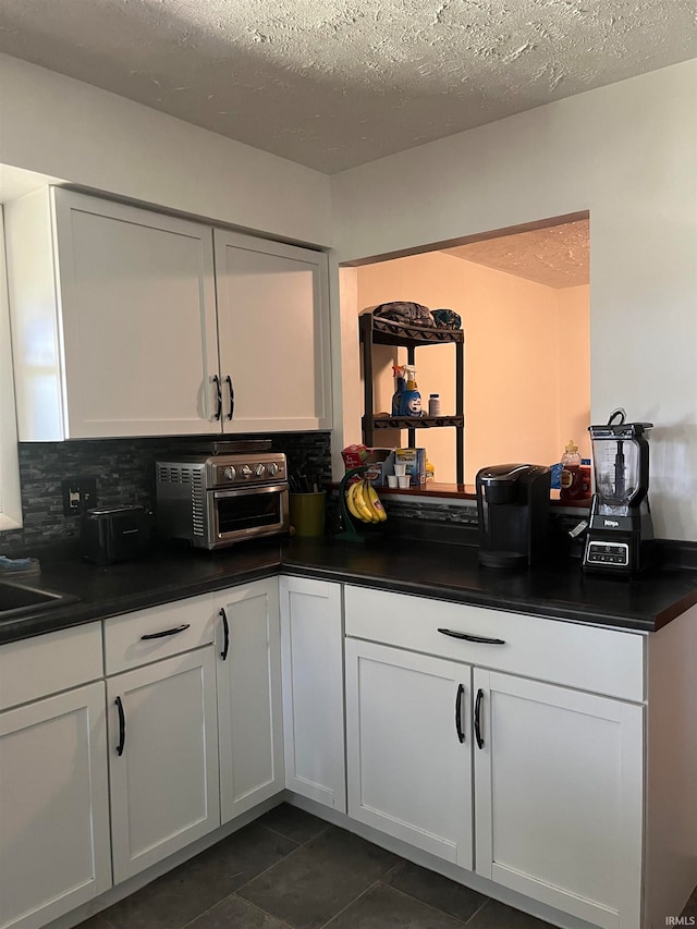 kitchen with dark tile patterned flooring, white cabinetry, a textured ceiling, and tasteful backsplash