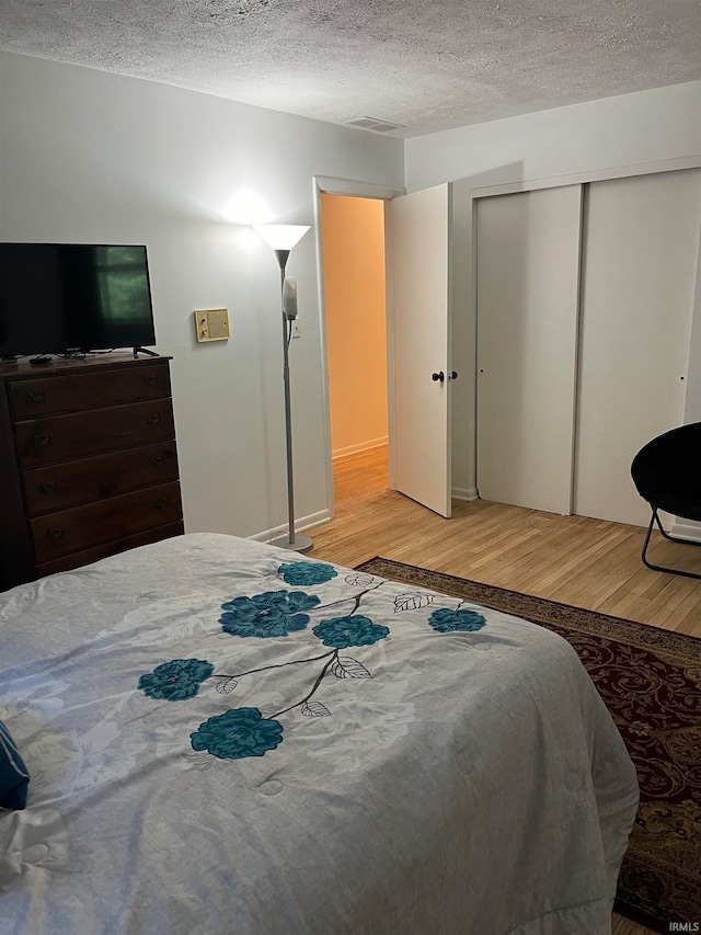 bedroom with a closet, a textured ceiling, and light hardwood / wood-style flooring