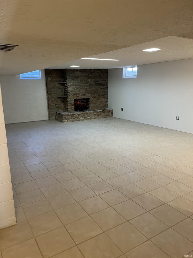 basement with light tile patterned flooring and a stone fireplace