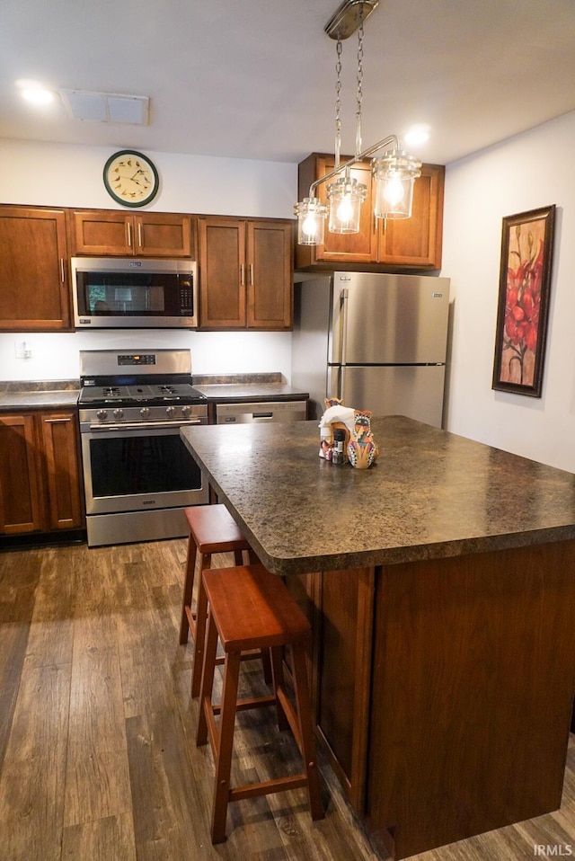 kitchen with hanging light fixtures, a breakfast bar, dark wood-type flooring, appliances with stainless steel finishes, and a center island