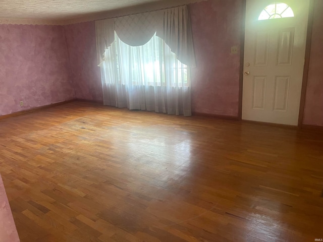 empty room with wood-type flooring, a textured ceiling, and a healthy amount of sunlight