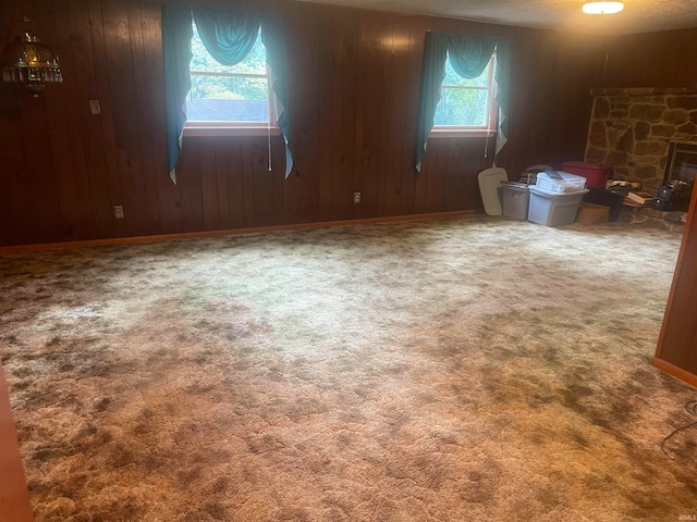 unfurnished living room featuring carpet floors, a stone fireplace, and wooden walls