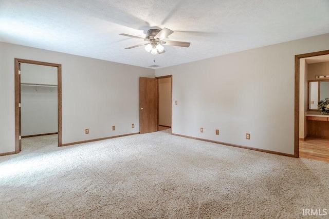 unfurnished bedroom with a spacious closet, baseboards, light colored carpet, and a textured ceiling