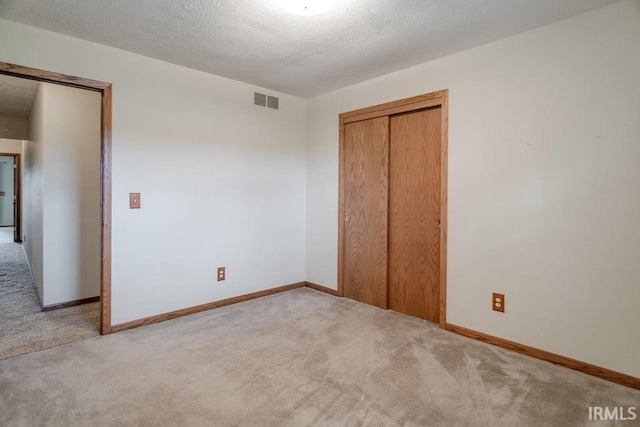 unfurnished bedroom featuring a closet, carpet flooring, a textured ceiling, visible vents, and baseboards