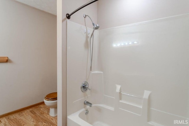 bathroom featuring wood-type flooring, a textured ceiling, toilet, and washtub / shower combination