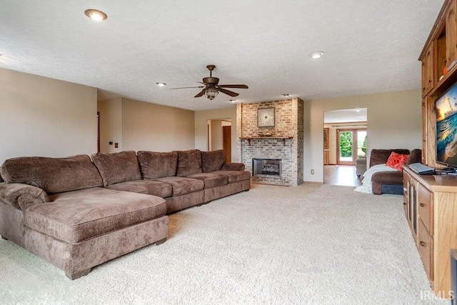 living room with light colored carpet, a fireplace, ceiling fan, and a textured ceiling
