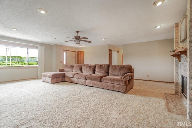 living room with a brick fireplace, ceiling fan, light colored carpet, and a textured ceiling