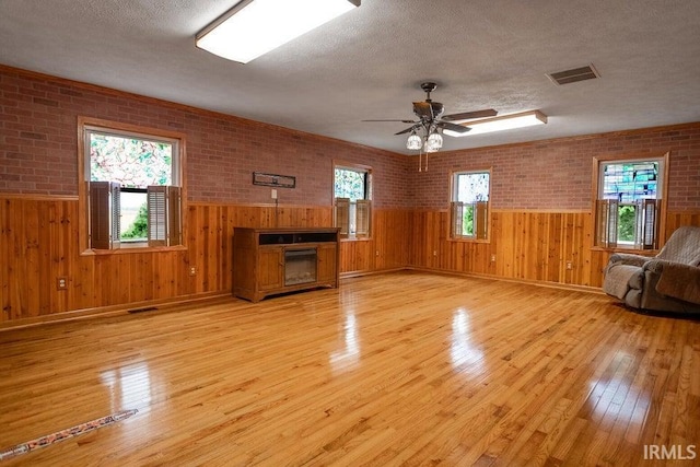 unfurnished living room with light hardwood / wood-style floors, ceiling fan, brick wall, and a healthy amount of sunlight