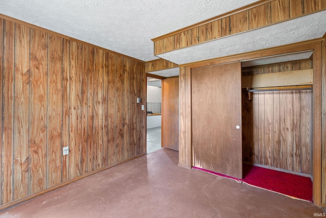 unfurnished bedroom featuring a textured ceiling, wooden walls, a closet, and concrete floors