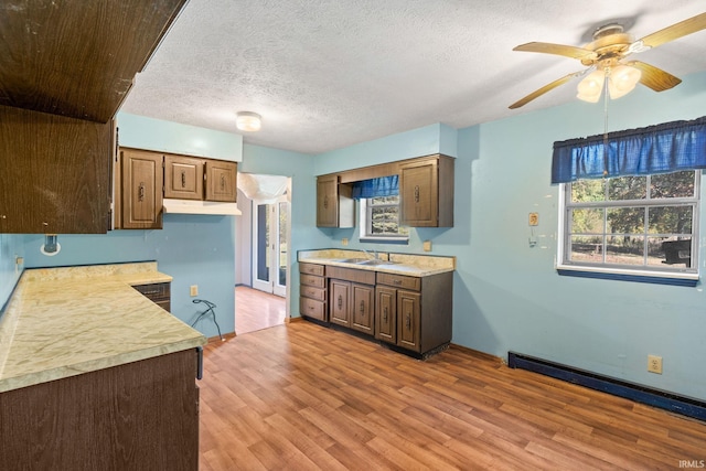 kitchen featuring ceiling fan, baseboard heating, sink, light hardwood / wood-style flooring, and a textured ceiling