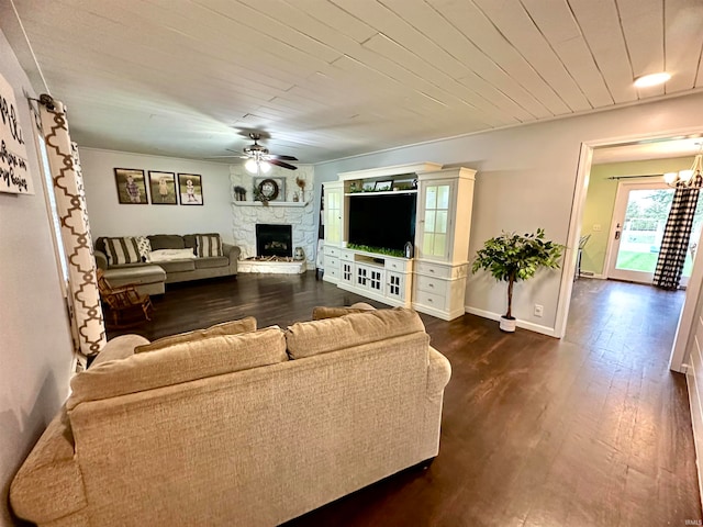 living room with ceiling fan with notable chandelier, a stone fireplace, and dark hardwood / wood-style flooring