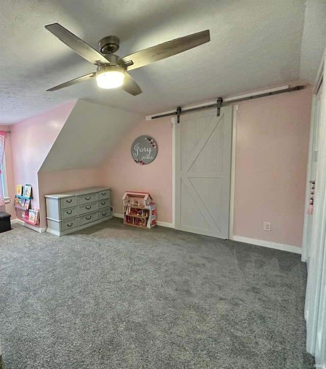 interior space with a textured ceiling, lofted ceiling, a barn door, carpet, and ceiling fan