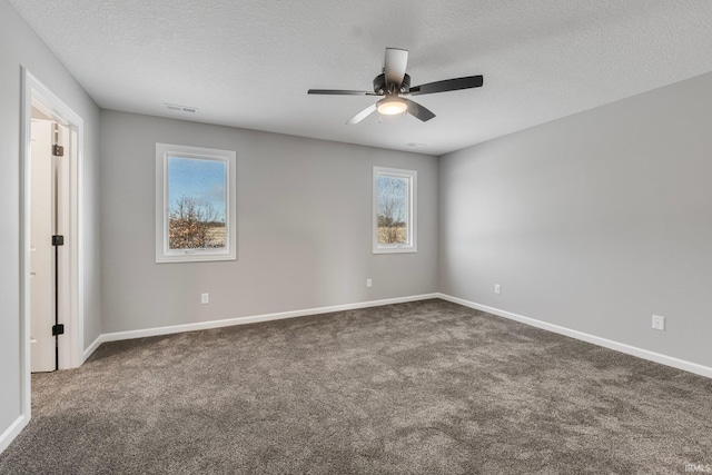 unfurnished room with a textured ceiling, dark carpet, and plenty of natural light