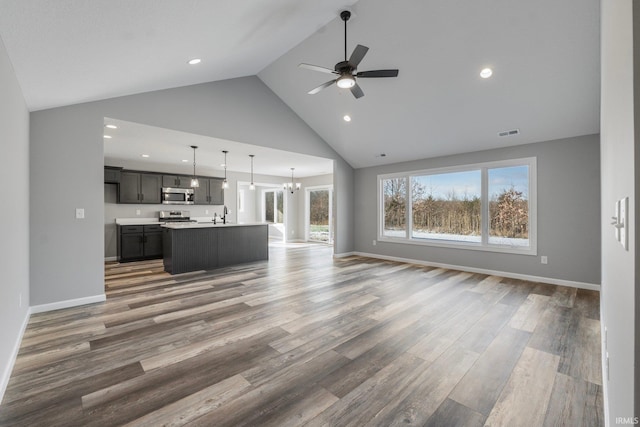 unfurnished living room with ceiling fan with notable chandelier, dark hardwood / wood-style floors, high vaulted ceiling, and sink