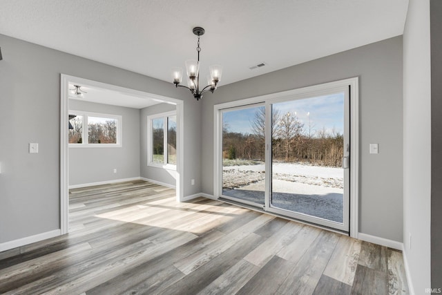 unfurnished dining area with hardwood / wood-style floors, a textured ceiling, and a notable chandelier