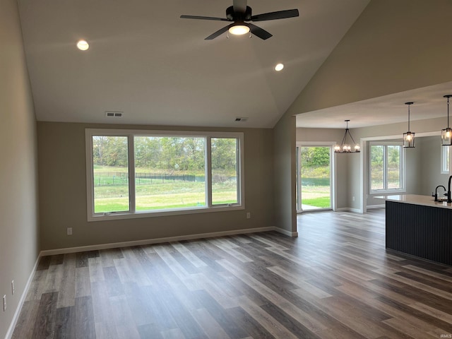 unfurnished living room featuring dark hardwood / wood-style floors, vaulted ceiling, and ceiling fan with notable chandelier