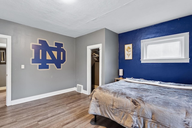 bedroom with hardwood / wood-style floors, a walk in closet, and a textured ceiling