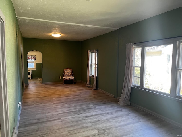 unfurnished room with arched walkways, a textured ceiling, baseboards, and wood finished floors