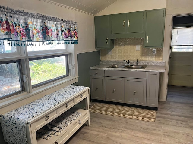 kitchen with green cabinetry, vaulted ceiling, sink, and light hardwood / wood-style flooring