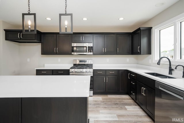 kitchen with appliances with stainless steel finishes, hanging light fixtures, light hardwood / wood-style floors, and sink