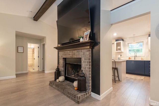 living room with lofted ceiling with beams, a brick fireplace, hardwood / wood-style floors, and sink