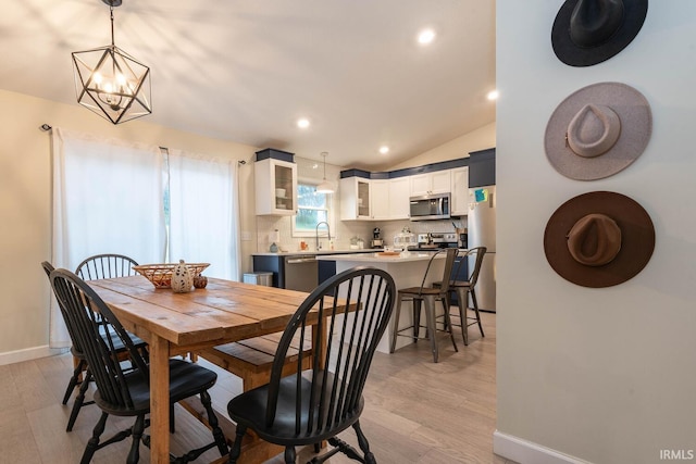 dining space with sink, lofted ceiling, a chandelier, and light hardwood / wood-style floors