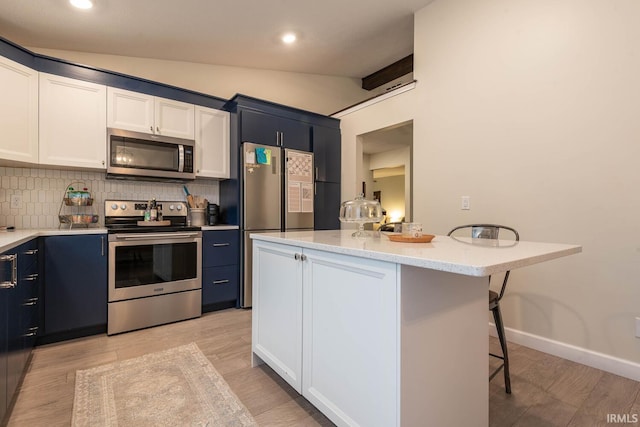 kitchen with appliances with stainless steel finishes, light hardwood / wood-style floors, vaulted ceiling, white cabinets, and a kitchen bar