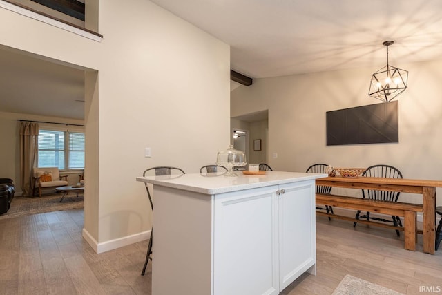 kitchen with lofted ceiling with beams, a notable chandelier, white cabinetry, hanging light fixtures, and light hardwood / wood-style flooring