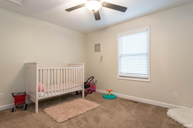 carpeted bedroom featuring ceiling fan and a nursery area